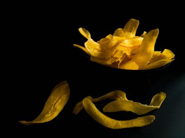 Siyah bir yüzeyde sarı muz cipsi