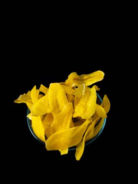 Muz cipsiyle dolu şeffaf bir cam kase siyah arka planda.