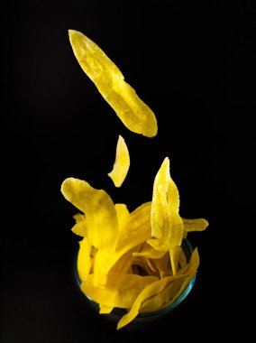 Muz cipsiyle dolu şeffaf bir cam kase siyah arka planda.