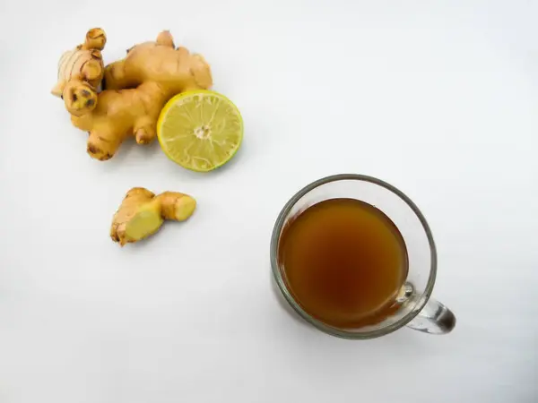 Sıcak zencefil suyuyla dolu şeffaf bir cam bardak beyaz bir yüzeye oturur.