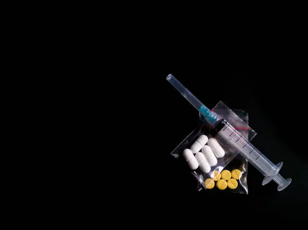 Siyah zemin üzerinde şeffaf bir şırınga ve uyuşturucu