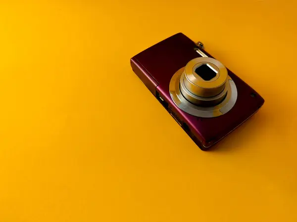 Metalik mor gövdeli kompakt dijital kamera koyu sarı arkaplanda oturur