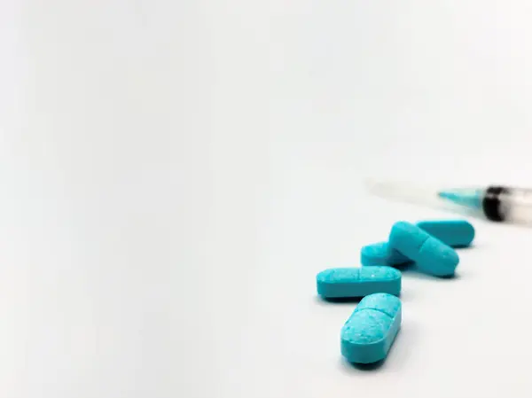 Boş plastik şırınga ve beyaz bir yüzeye mavi haplar.