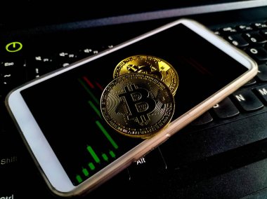 Bir akıllı telefon ve altın Bitcoin paraları dizüstü bilgisayarın klavyesine yerleştirilir.