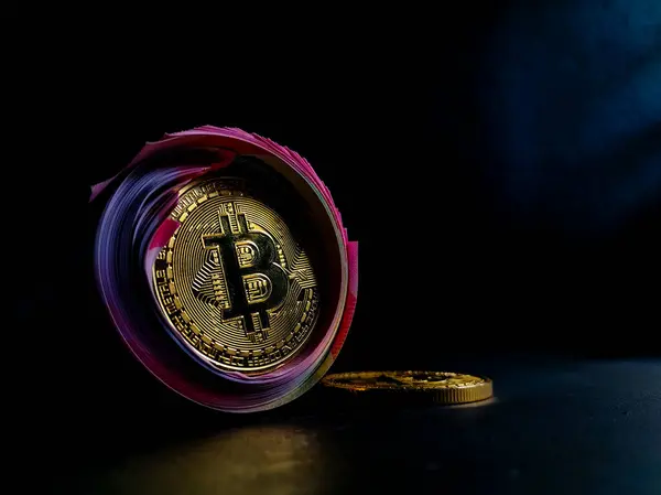 Bitcoin simgesi, karanlık bir yüzeyde yuvarlanan banknotlara dayanır. 
