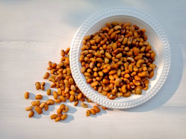 Bezelyeler (Vigna unguiculata) desenli beyaz bir kağıt tabağın etrafına saçılmıştır.. 