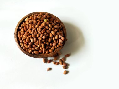 Çiğ fıstıkla dolu yuvarlak ahşap bir kase beyaz bir yüzeyde duruyor..