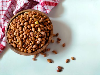 Çiğ fıstıkla dolu yuvarlak ahşap bir kase beyaz bir yüzeyde duruyor..