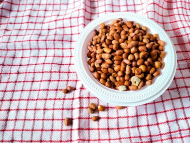 Çiğ fıstıkla dolu beyaz bir kase kırmızı ve beyaz kareli kumaşın üzerinde duruyor..