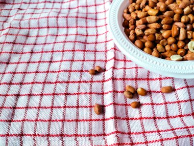Çiğ fıstıkla dolu beyaz bir kase kırmızı ve beyaz kareli kumaşın üzerinde duruyor..