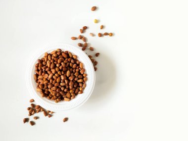 Kahverengi fıstıkla dolu beyaz bir kase beyaz bir yüzeye yerleştirilir.. 