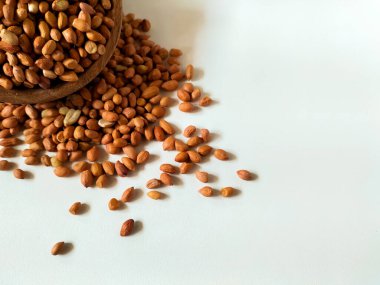 Çiğ fıstıkla dolu yuvarlak ahşap bir kase beyaz bir yüzeyde duruyor..