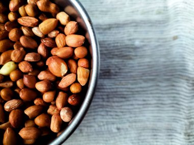 Doğal kırmızı-kahverengi kabuklarını gösteren çiğ fıstıkla dolu sığ metal bir kase..