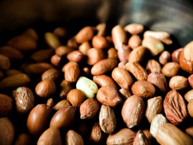 Doğal kırmızı-kahverengi kabuklarını gösteren çiğ fıstıkla dolu sığ metal bir kase..