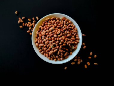 Beyaz bir kase koyu arka planda çiğ fıstıkla doludur.