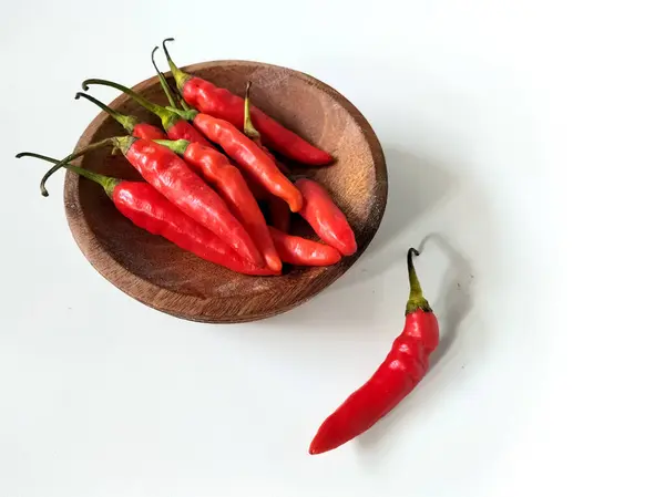 Kırmızı biberler beyaz bir yüzey üzerinde tahta bir kasede sergilenir..