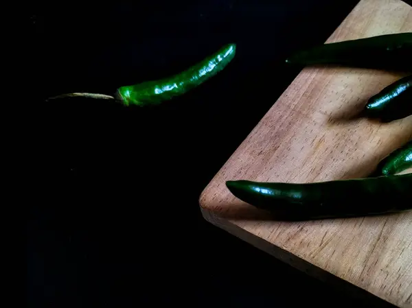 Açık ahşap kesme tahtasındaki yeşil biberler siyah arkaplanda dinleniyor 