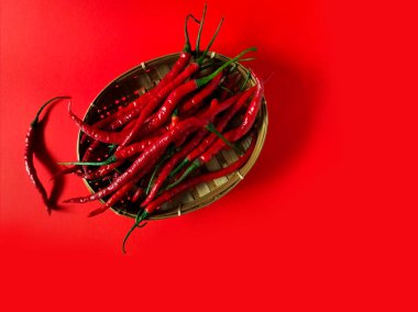 Kırmızı biberler kırmızı arka planda dokuma bambu sepetine konur.