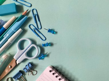 Açık mavi arka planda çeşitli okul malzemeleri düzenlenmiştir.