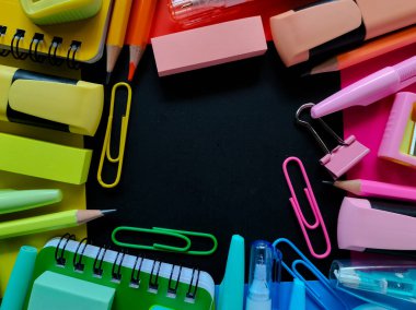 Siyah merkezi bir alana yerleştirilmiş rengarenk okul malzemeleri..