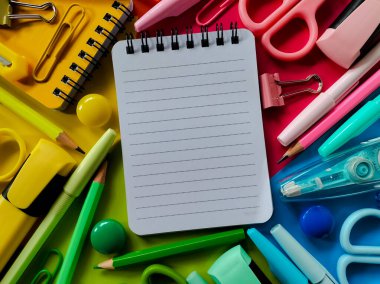 Çeşitli rengarenk okul gereçleri küçük, çizgili bir not defterini çevrelemiş.. 
