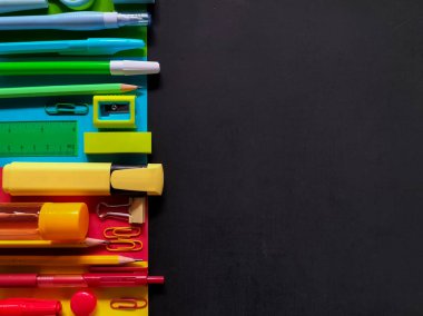 Siyah bir yüzeye yerleştirilmiş renkli okul malzemeleri.. 