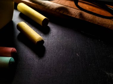 Renkli tebeşir çubukları, santimetre ve santimetre olarak işaretlenmiş ahşap bir cetvelle birlikte siyah bir yüzeye yerleştirilmiştir.. 
