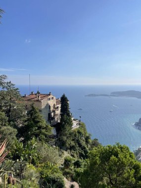 Uçurum kenarındaki binalar açık bir günde sakin bir mavi denize bakıyor. Akdeniz mimarisi, bereketli yeşillik ve sonsuz okyanus ufkunun yer aldığı çarpıcı bir kıyı manzarası..