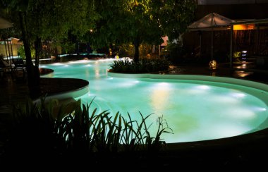 Gece havuzu. Işıklı su ve çevreleyen ağaçlar.