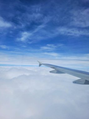Aşağıdaki kabarık bulutlarla mavi gökyüzünün çarpıcı görüntüsü, bir uçak penceresinden çekildi. Kanat, özgürlük ve macera duyguları uyandıran engin, berrak arka plana karşı duruyor..