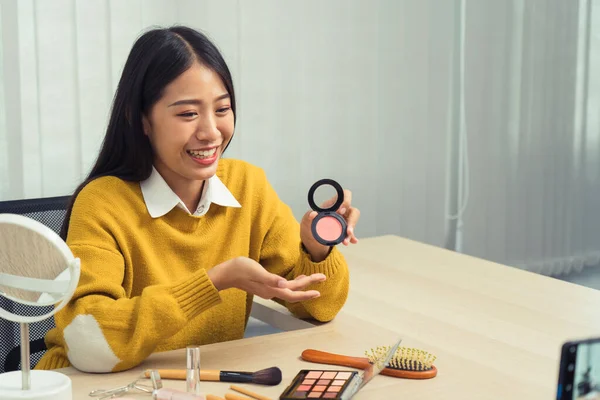 若いアジアの女性は 自宅で携帯電話のカメラを使用して化粧品に彼女のブログのためのビデオを作ると美容製品について自分自身をVlogging — ストック写真