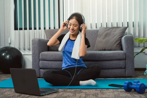 stock image Asian beautiful young woman using laptop and headphones listen music while practicing exercise yoga at home.