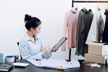 Asyalı girişimci tabletiyle depodaki kalan giysileri kontrol ediyor..