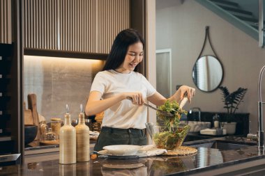 Asyalı ev hanımı mutfak tezgahında salata yapmak için taze sebze hazırlıyor..