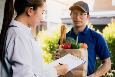 Asyalı kadın ürünü kontrol ediyor ve sipariş makbuzunu online süpermarketten imzalıyor..