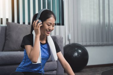 Laptop ve kulaklık kullanan Asyalı güzel genç kadın evde egzersiz yaparken müzik dinliyor..