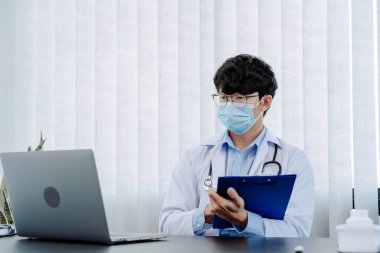 Doktor ofiste oturmuş, maske takarken dizüstü bilgisayarla uğraşıyordu..