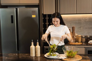 Asyalı ev hanımı mutfak tezgahında salata yapmak için taze sebze hazırlıyor..