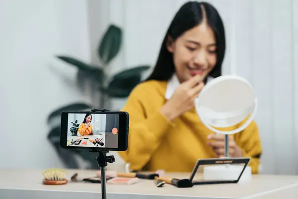若いアジアの女性は 自宅で携帯電話のカメラを使用して化粧品に彼女のブログのためのビデオを作ると美容製品について自分自身をVlogging ストック画像