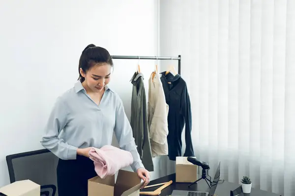 アジアの起業家は 顧客への配達のために紙箱で販売することができる彼女の服を準備しています ロイヤリティフリーのストック画像