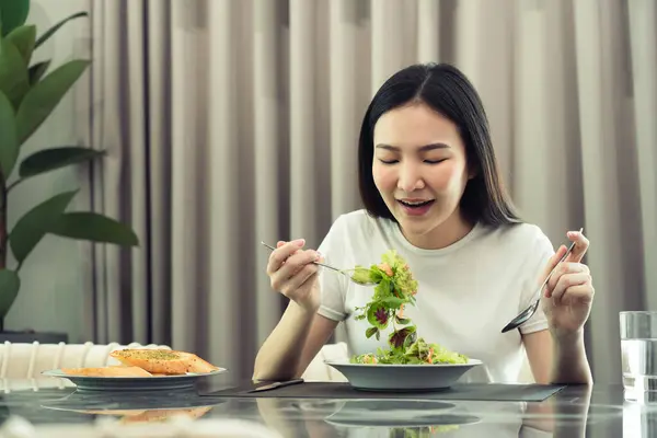アジアの若い女性は 彼女が皿の上にサラダをスクープし 喜んで家で食べるように笑顔 ロイヤリティフリーのストック写真