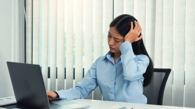 Asian woman sitting and working has a headache. clipart