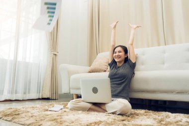 Asyalı kadın dizüstü bilgisayarıyla işini bitirirken kağıtları oturma odasına atıyor..