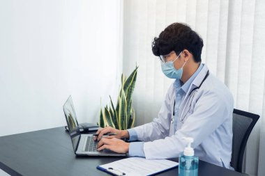 Doktor ofiste oturmuş, maske takarken dizüstü bilgisayarla uğraşıyordu..