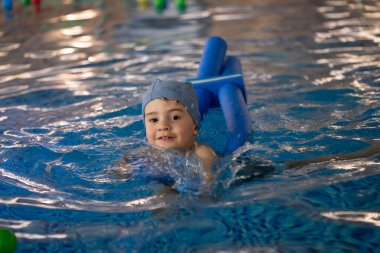 Küçük çocuk mavi yüzme cihazıyla yüzmeyi öğreniyor. Kapalı bir havuzda, su güvenliğini ve eğlencesini arttırıyor.