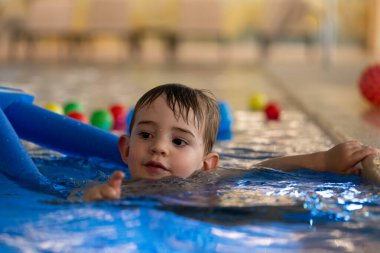 Mutlu çocuk neşeyle yüzüyor ve serinletici bir havuzda canlı yüzen oyuncaklarla oynuyor, yaz tatili eğlencesini kucaklıyor.