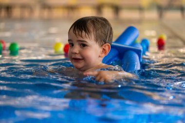 Küçük çocuk, kapalı havuzda yüzme cihazıyla yüzme dersinden, su güvenliğini ve erken çocukluk gelişimini teşvik etmekten hoşlanıyor