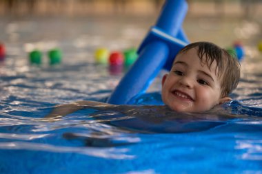 Mutlu çocuk yüzmeyi öğreniyor ve yüzme havuzunda renkli yüzen toplarla gülümsüyor.