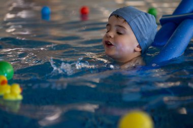 Küçük çocuk yüzme dersleri almaktan, yüzme aleti kullanmaktan ve havuzda renkli oyuncaklarla oynamaktan hoşlanıyor.