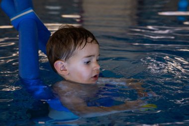 Küçük çocuk yüzme dersleri almaktan, kapalı havuz ortamında renkli yüzme araçlarıyla oynamaktan ve öğrenmekten hoşlanıyor.